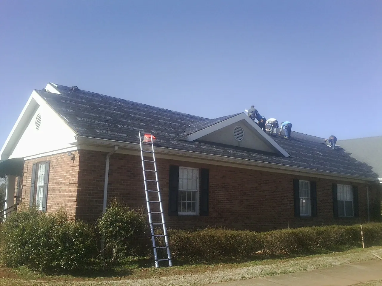 Crew tearing shingles off a brick ranch roof with a ladder set — Emergency Roof Repair work by our crew in Medusa