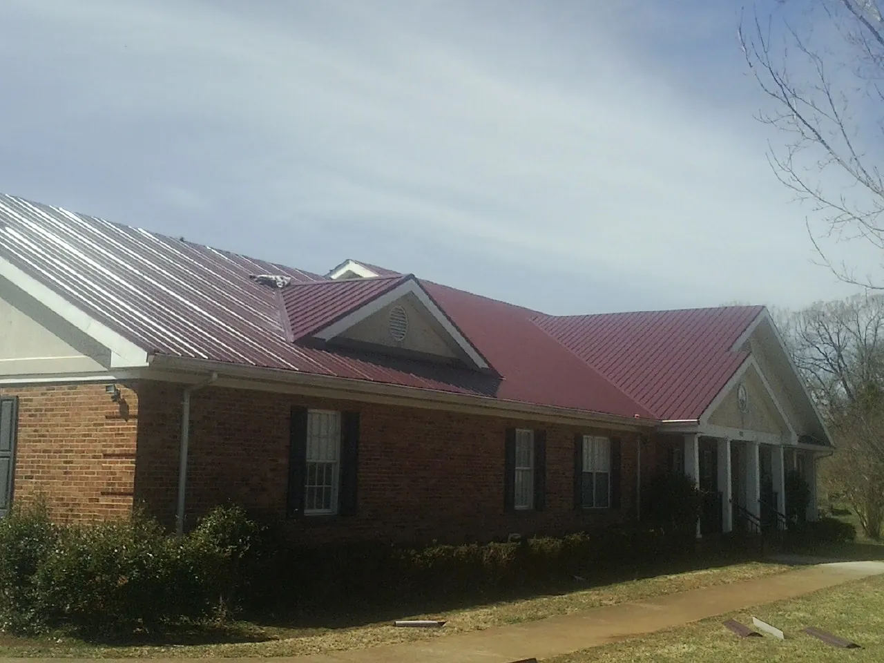Red metal roof with gabled entries on a long brick building, from a Hail Damage Roof Repair job in Medusa