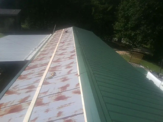 Old rusted panels beside newly installed green metal roofing — Wind Damage Roof Repair by Roofing Brothers in Medusa