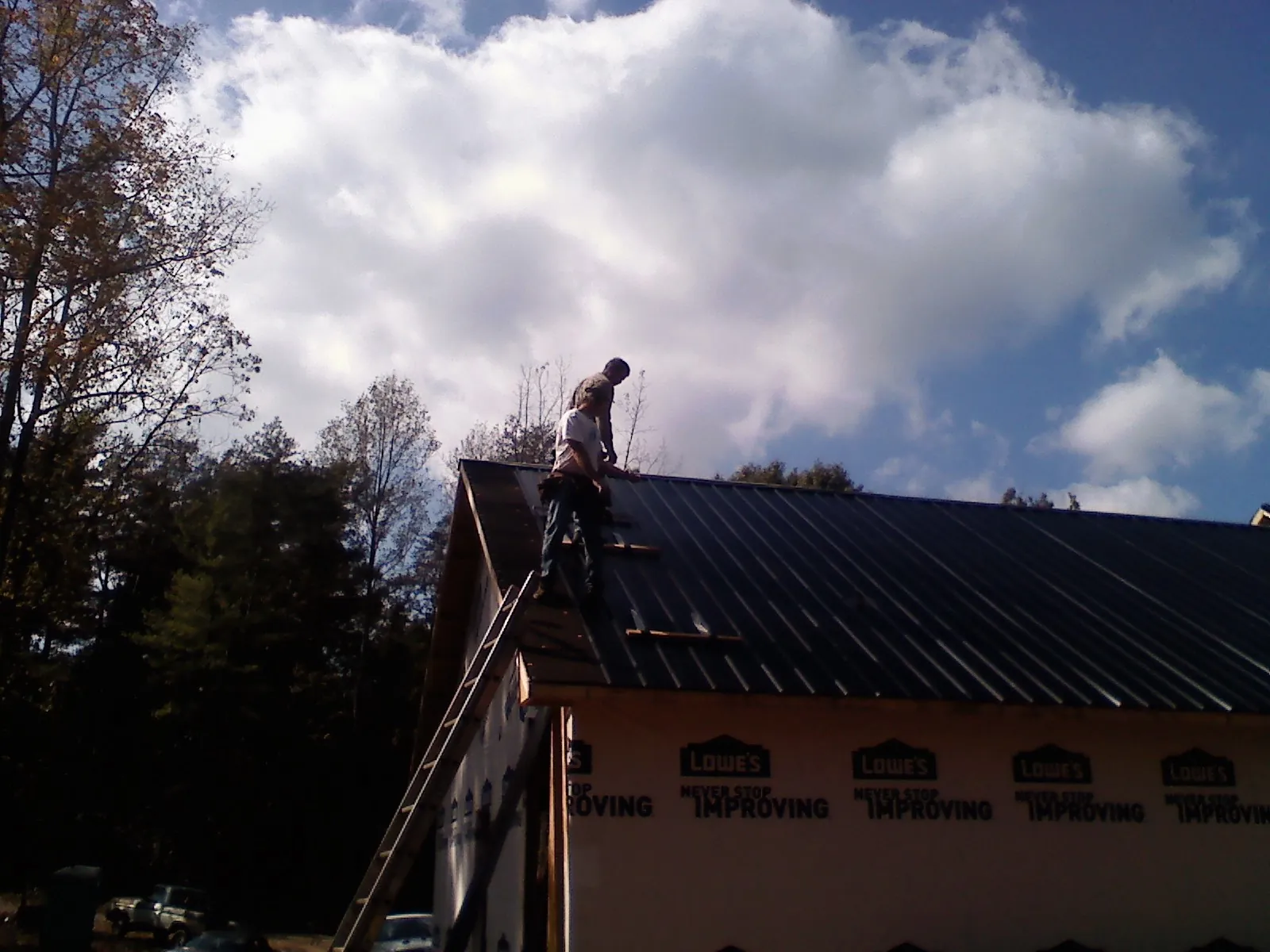Roofer fastening dark metal panels high against a cloudy sky, from a Roof Inspection job in Medusa