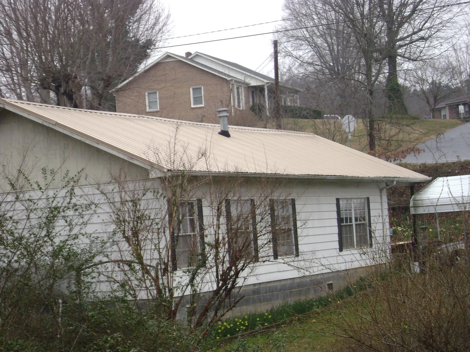 Tan metal roof on a white sided house set into a hillside — Commercial Roofing by Roofing Brothers in Medusa